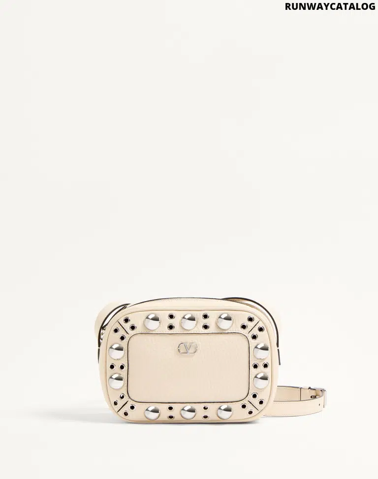 A Valentino Garavani Nellcôte chain shoulder bag in grainy calfskin leather, adorned with ball studs and rivets. Features a VLogo Signature metallic accent, palladium-finish hardware, zipper closure, and an adjustable leather strap for shoulder or cross-body wear. The suede-lined interior includes a card pocket for storage.