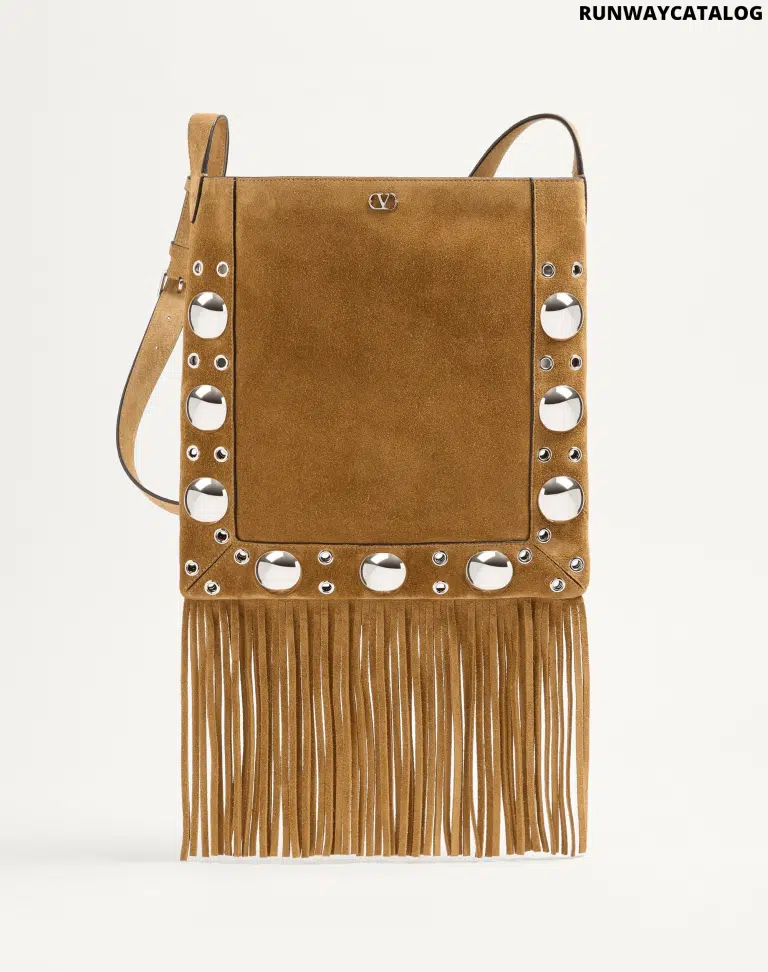 A Valentino Garavani Nellcôte suede shoulder bag with long fringe details, studded trim, and an adjustable suede strap for crossbody or shoulder wear. Features palladium-finish hardware and a VLogo metallic accent.