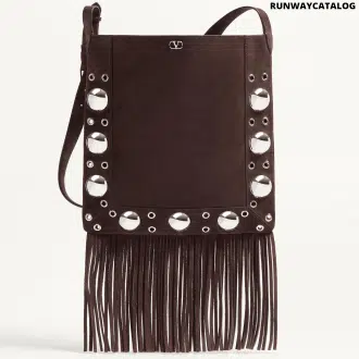 A Valentino Garavani Nellcôte suede shoulder bag with bohemian fringe, studded trim, and an adjustable suede strap for crossbody or shoulder wear. Features palladium-finish hardware and a VLogo metallic accent.