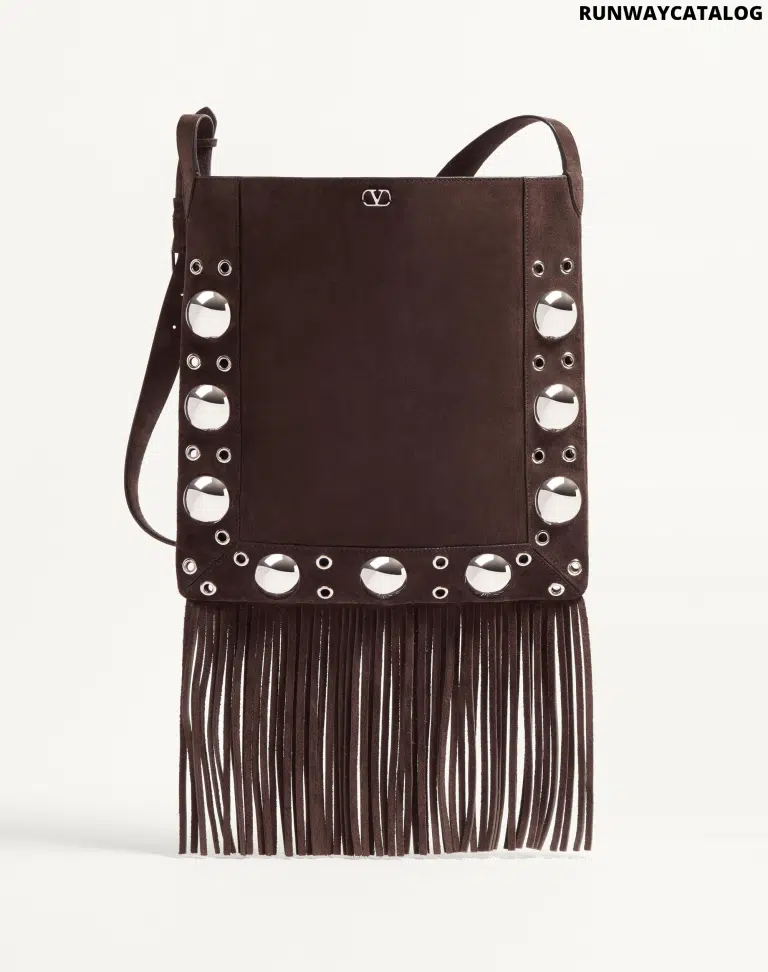 A Valentino Garavani Nellcôte suede shoulder bag with bohemian fringe, studded trim, and an adjustable suede strap for crossbody or shoulder wear. Features palladium-finish hardware and a VLogo metallic accent.